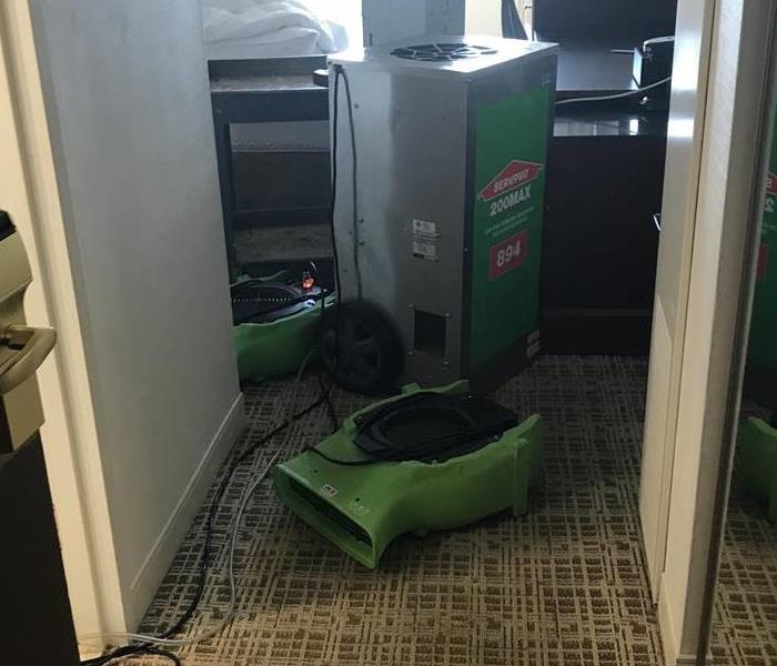 Green air mover on the floor in front of a dehumidifier. 